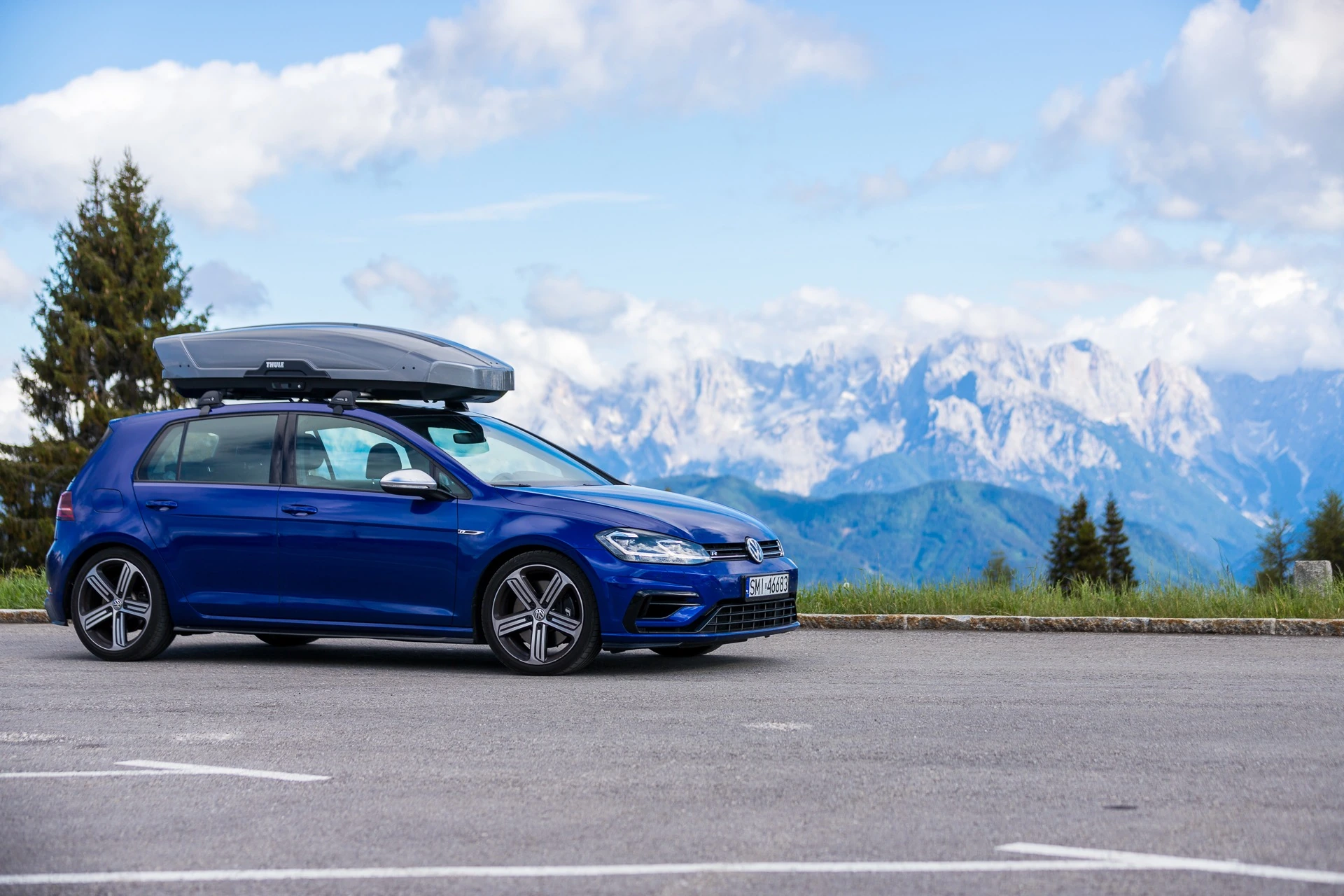 Niebieski Volkswagen Golf z boxem dachowym Thule Motion XT XL w kolorze tytan – szerokie ujęcie górskie